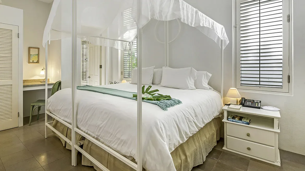 Elegant four-poster bed with a white canopy and white bedding in a tropical villa.