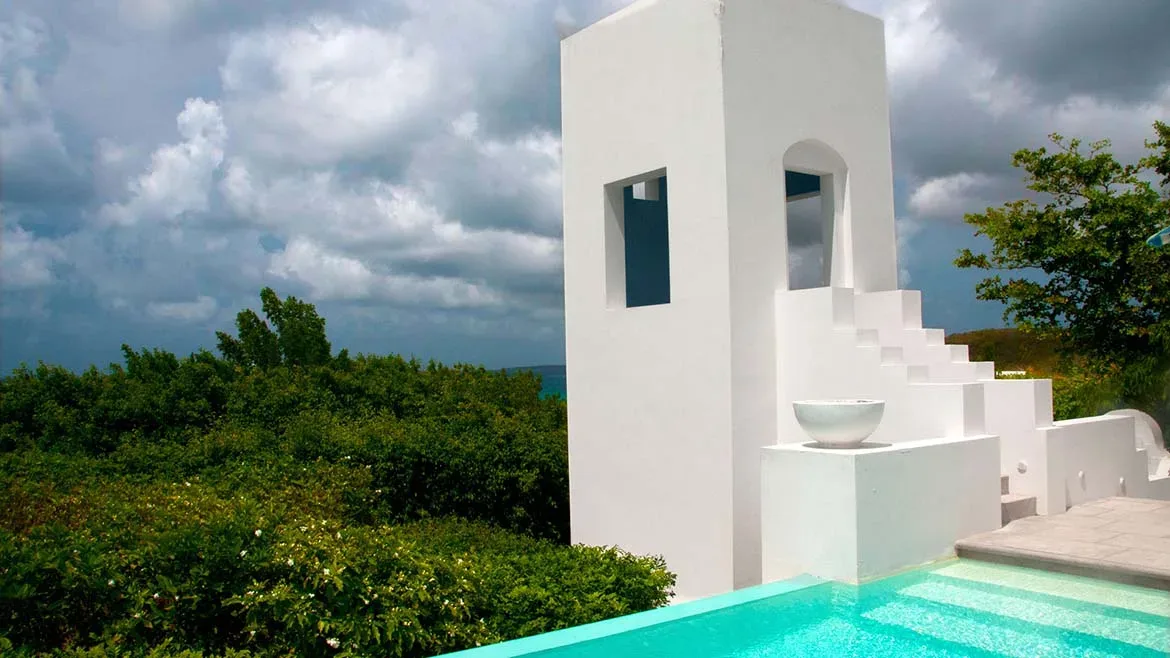 Minimalist white geometric architecture and outdoor stairs next to a turquoise pool under a cloudy sky.