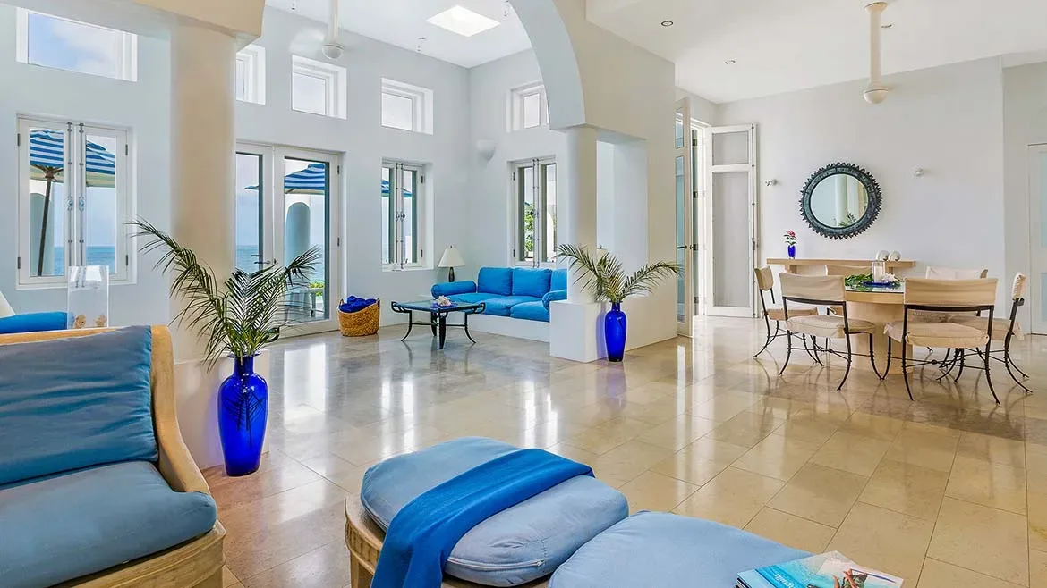 Bright white living room with blue sofas, a blue glass vase, and a dining area with a round mirror on the wall.