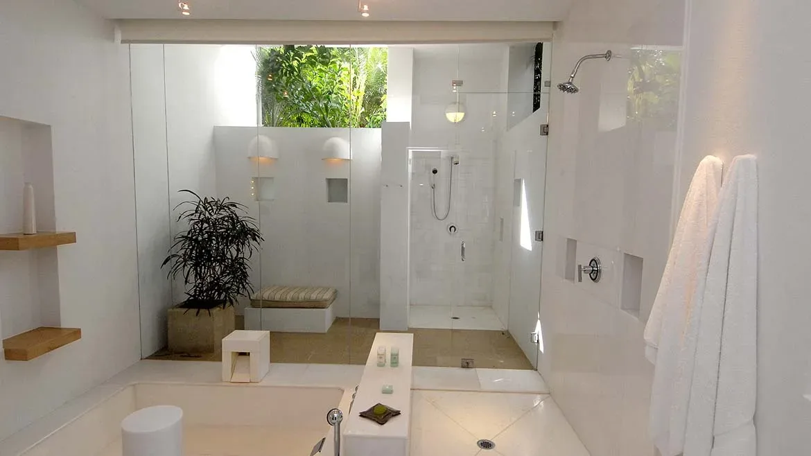 A minimalist all-white luxury bathroom featuring a glass walk-in shower and built-in shelving.