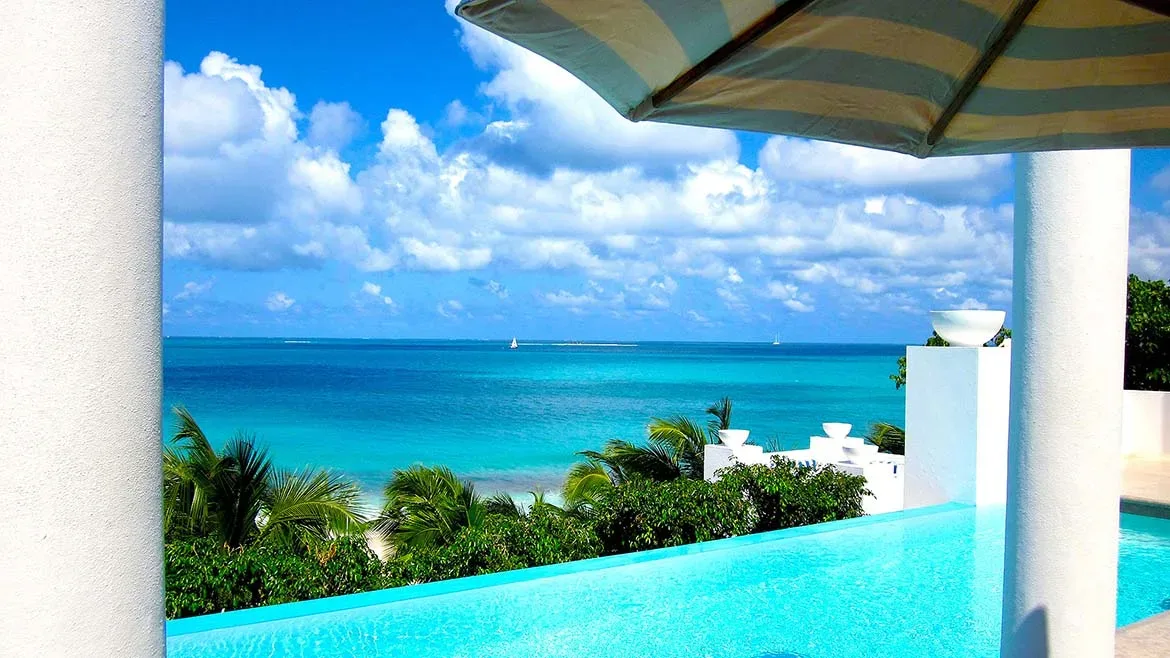 View from the infinity pool looking out across the bright blue ocean toward the horizon under a cloudy sky.