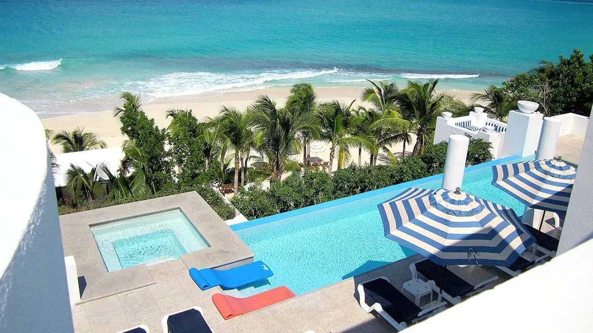 Aerial view of the villa's luxury pool area featuring blue and orange loungers, a hot tub, and striped umbrellas.