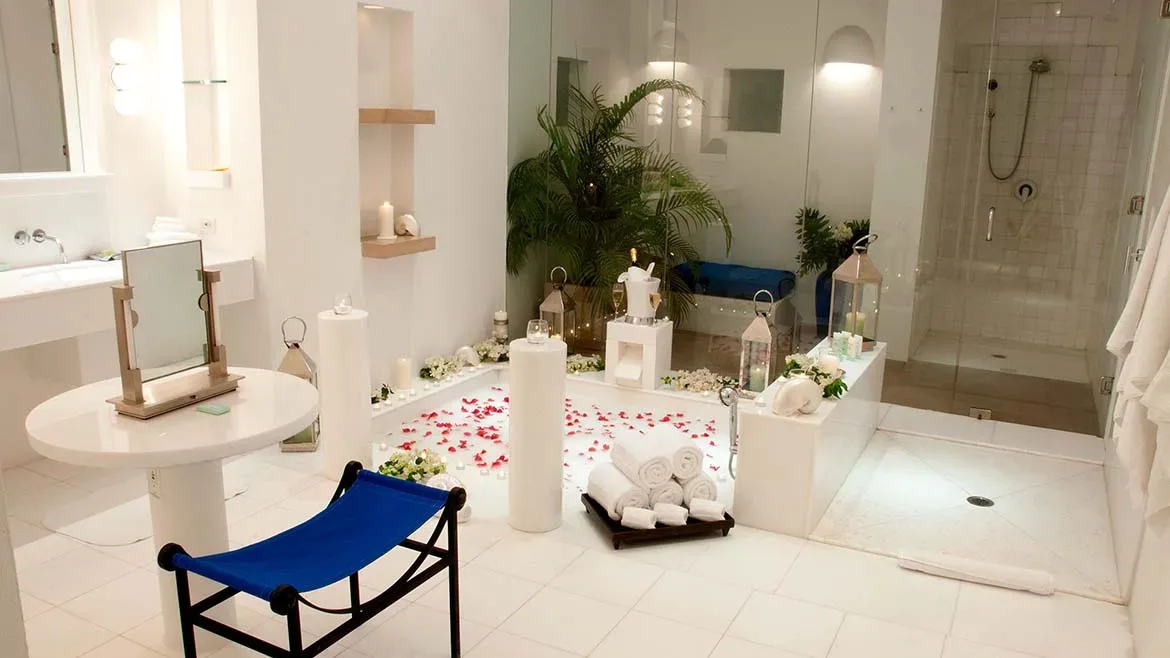 A luxurious white spa bathroom decorated with red flower petals, white towels, and candles.
