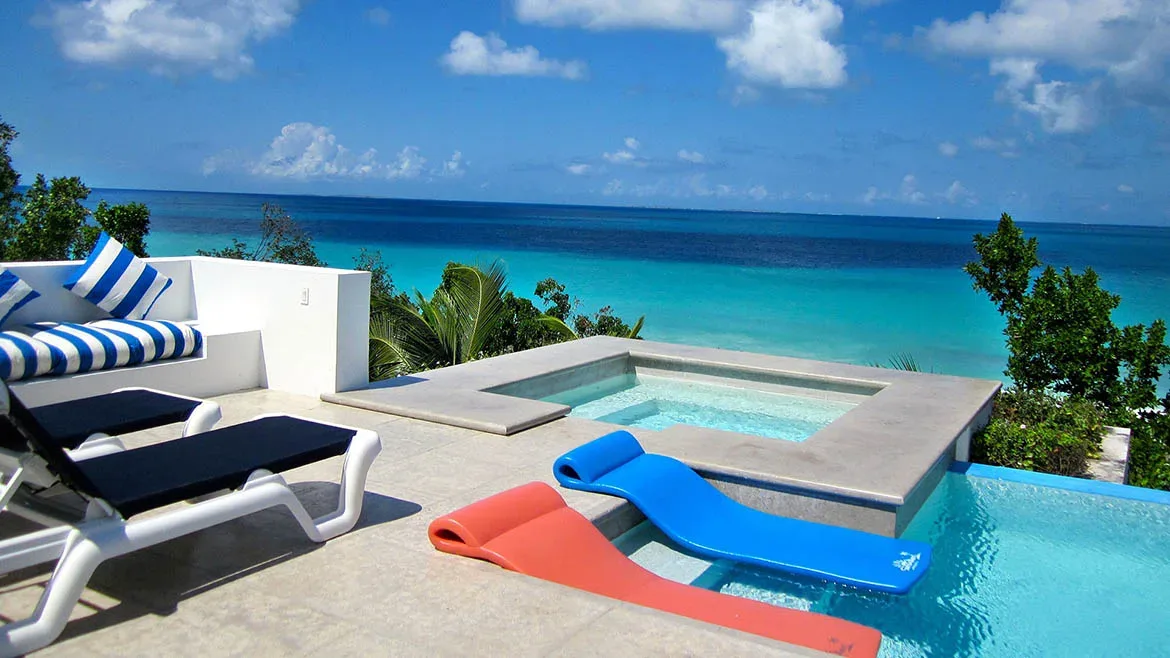 Modern poolside terrace with colorful lounge chairs and a square plunge pool overlooking the Caribbean Sea.