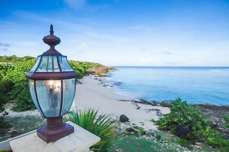 A decorative outdoor lantern in the foreground with a scenic view of the white sand beach and blue ocean.