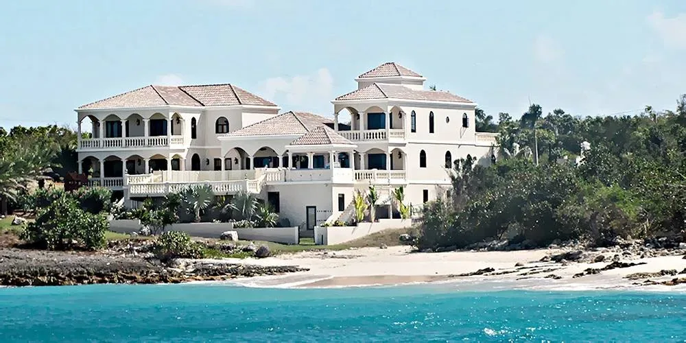 Beachfront view of a multi-story white villa with arched balconies and terracotta roofs.
