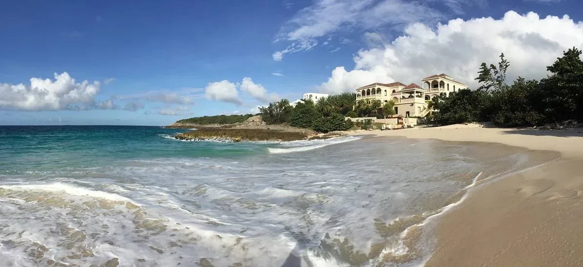 Wide shot of Villa Sandcastle's Mediterranean-style architecture on a white sandy beach with turquoise ocean waters.