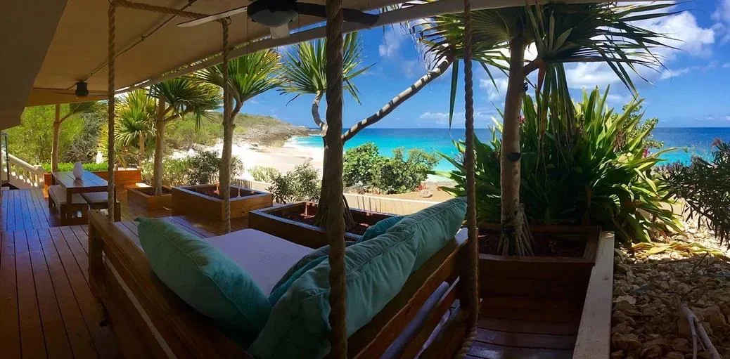 A comfortable outdoor daybed with light blue cushions inside a shaded gazebo overlooking the ocean.