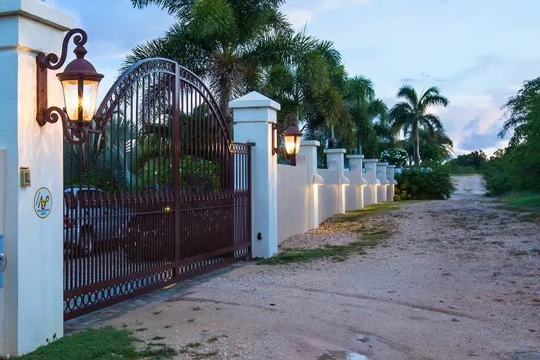 The gated entrance to Villa Sandcastle featuring a brown wrought iron gate, white pillars, and glowing lanterns.
