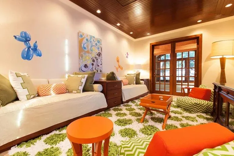 Colorful guest bedroom featuring a plush green and white shag rug, orange accents, and eclectic wall art.