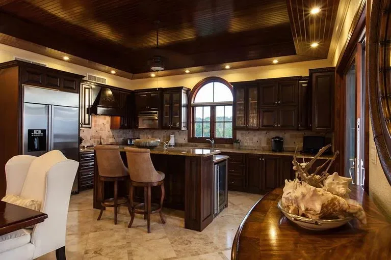 Luxurious kitchen featuring dark wood cabinets, a large center island with leather bar stools, and stainless steel appliances.