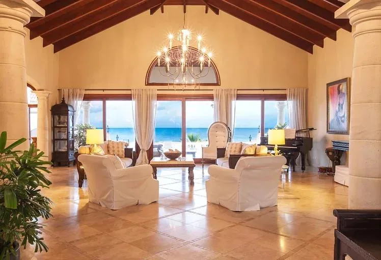 Spacious living room with white sofas, a grand chandelier, and open-concept access to a view of the turquoise ocean.