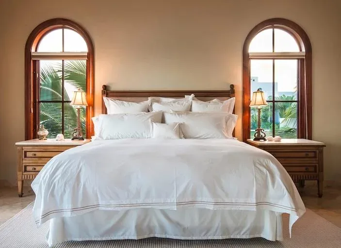 Elegant master bedroom with a king-sized bed, white linens, and arched windows.