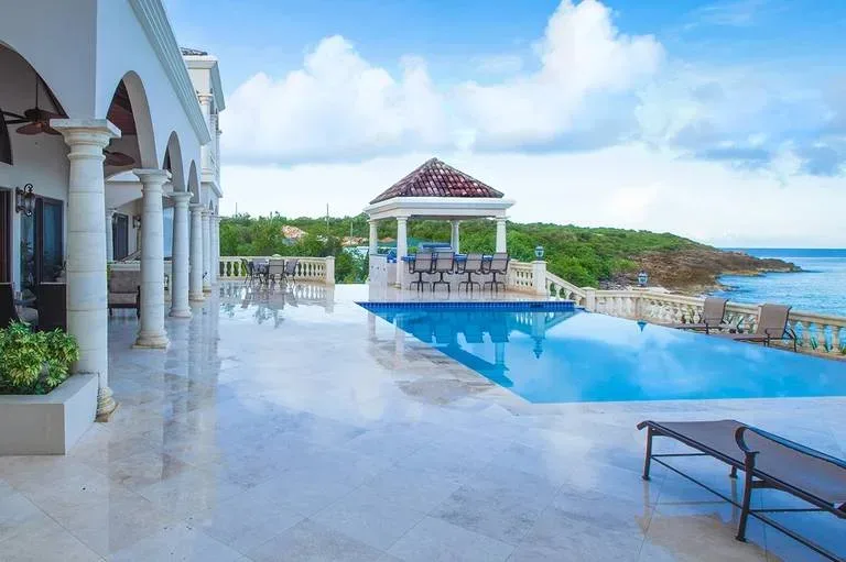 Luxury pool terrace with a large infinity pool, poolside lounge chairs, and a poolside bar under a gazebo.