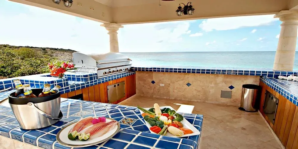 An outdoor poolside kitchen and bar with blue tiled countertops, a grill, and fresh food prepared for guests.
