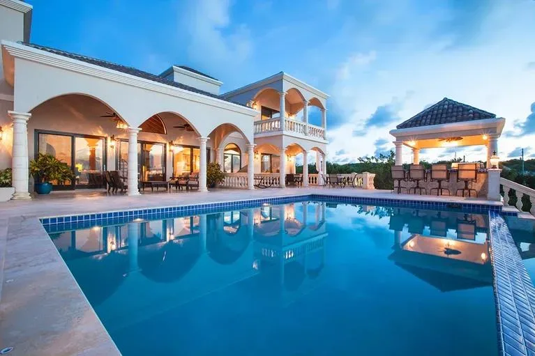 A luxury swimming pool reflecting the architecture of the villa and a poolside gazebo at twilight.