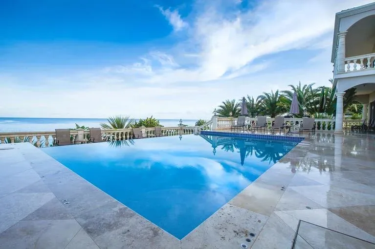 A luxury swimming pool with a white stone balustrade overlooking the turquoise waters of Limestone Bay.