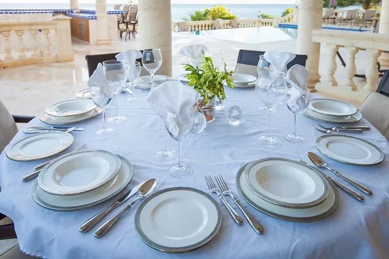 An elegantly set dining table with white linens and glassware on the villa's terrace overlooking the pool.