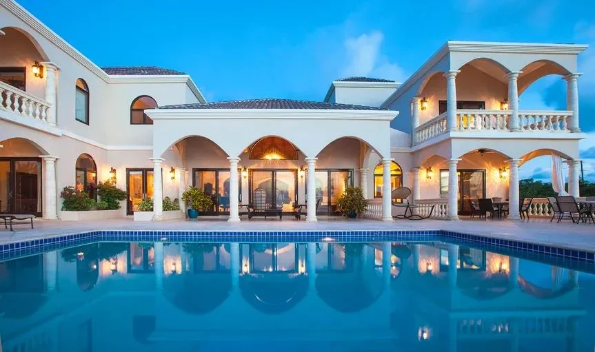 The grand arched facade of Villa Sandcastle with a sparkling blue swimming pool in the foreground.