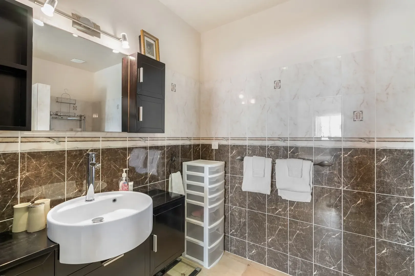 A modern bathroom with vessel sink, dark wood vanity, and marble-effect wall tiles — spa-style elegance.