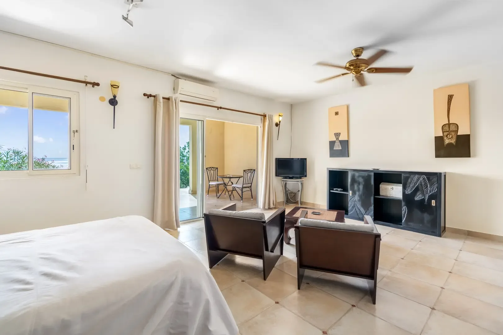 A bright bedroom with sliding glass doors opening to a private terrace with ocean views — indoor-outdoor living.