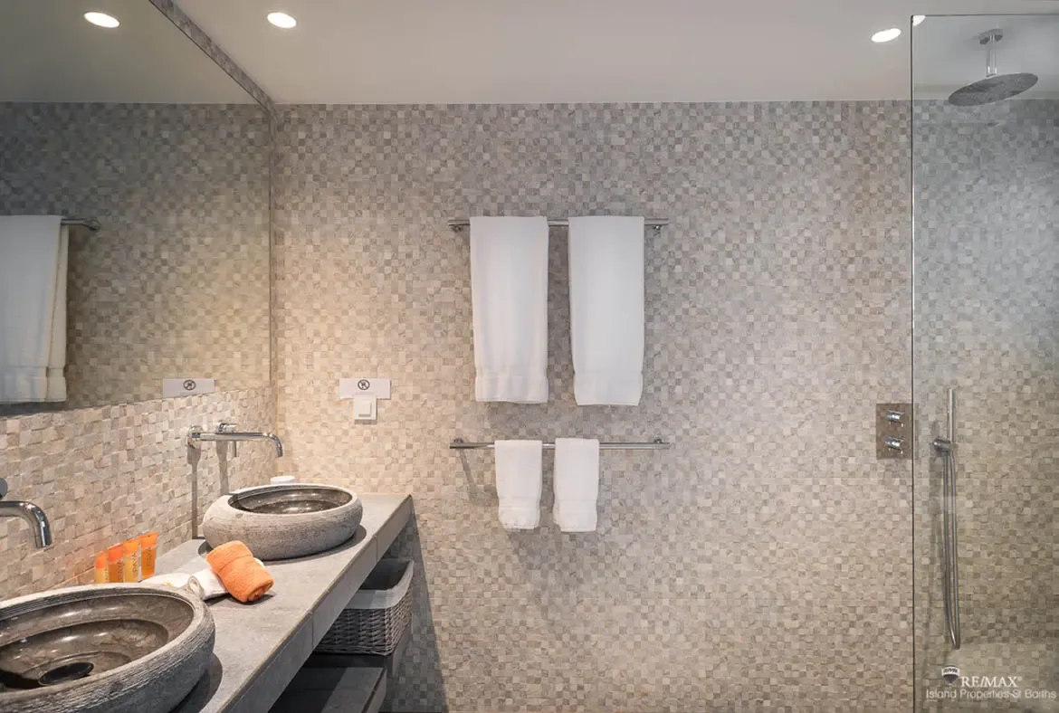 A spa-inspired bathroom with stone vessel sinks and glass-enclosed rain shower — pamper yourself in Caribbean luxury.