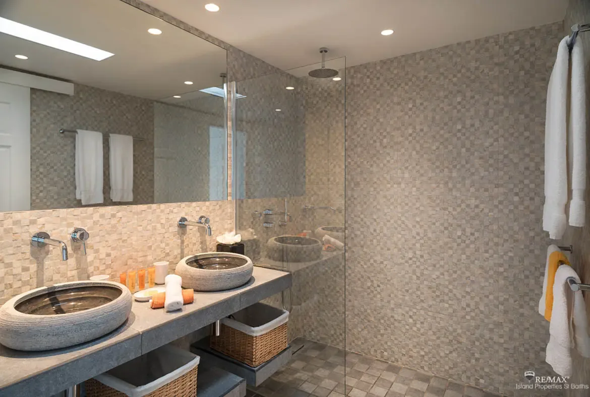 A modern bathroom with stone vessel sinks and glass-enclosed rain shower — spa-quality luxury in your Caribbean retreat.