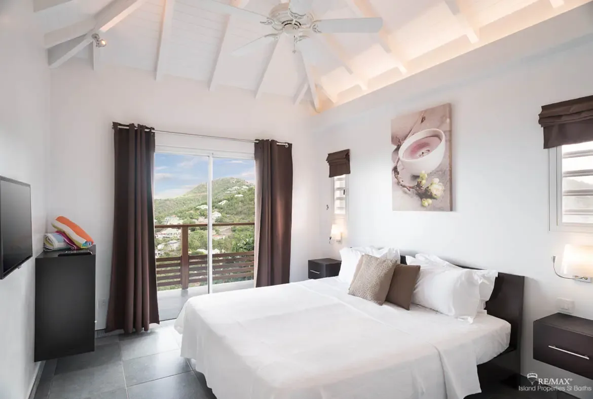 A serene bedroom with vaulted cathedral ceiling and sliding doors to your private balcony — wake up to Caribbean hill views.