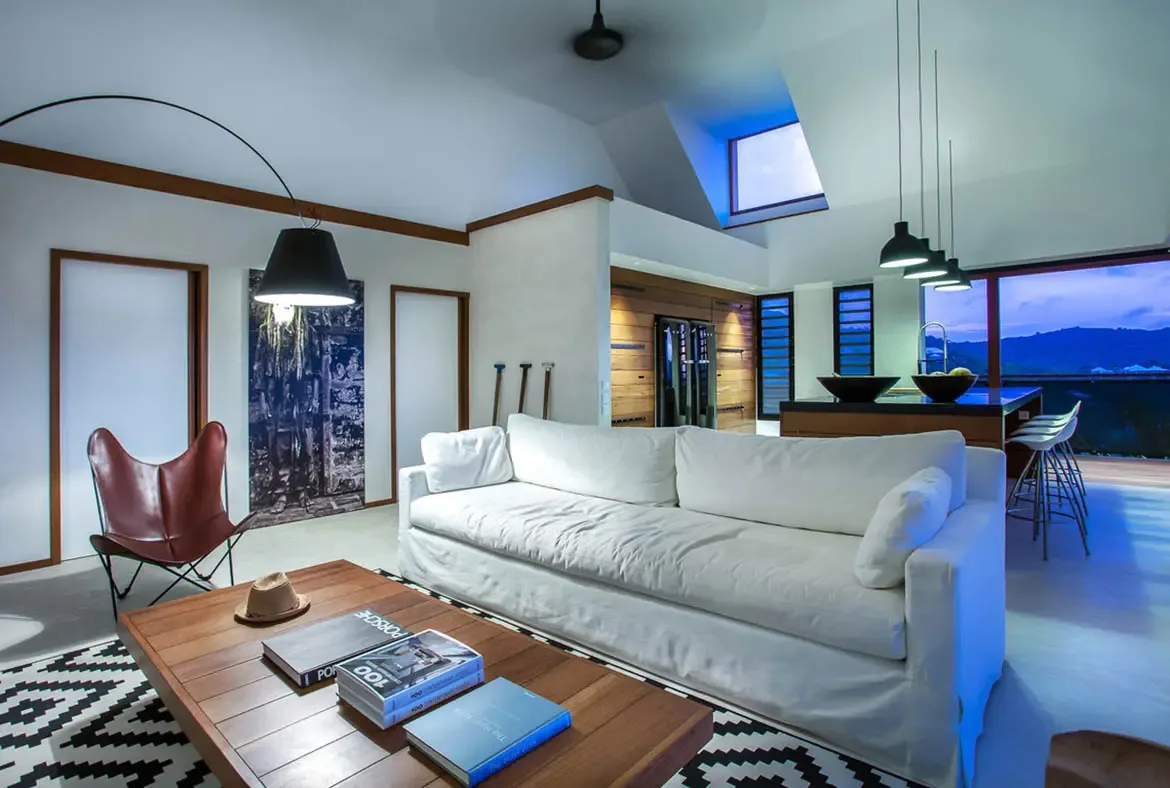 A dark wood bed with white linens sits beside open glass doors, where a private terrace with tropical greenery and a garden view invites relaxation.