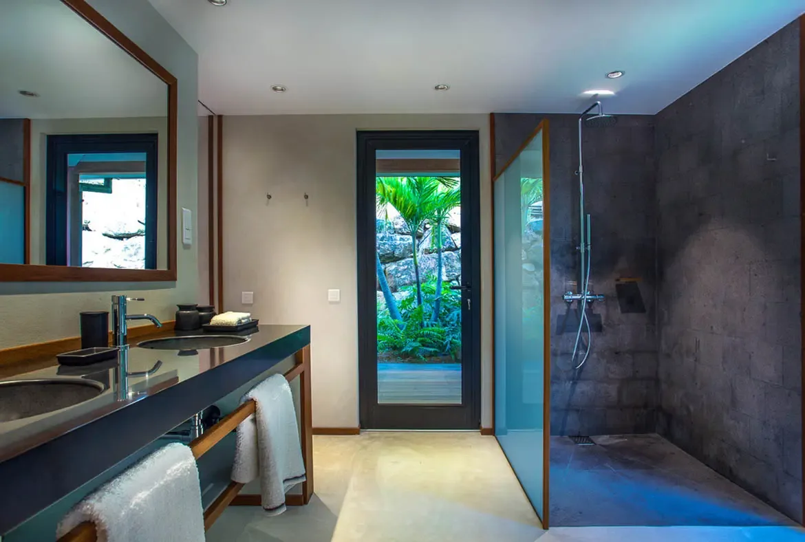 Two white beds with matching linens sit before open glass doors, where a private terrace with pink bougainvillea and tropical gardens invites relaxation.
