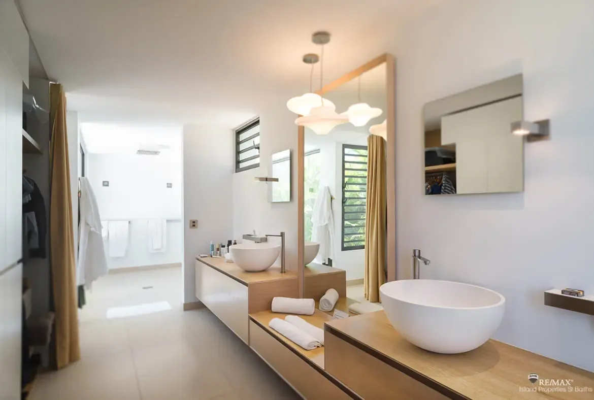 A floating wood double vanity with sculptural vessel sinks and soft pendant lighting gives this bathroom a calm, polished feel. Clean lines, warm textures, and an open dressing area beyond create the kind of space that makes getting ready feel unhurried and luxurious.