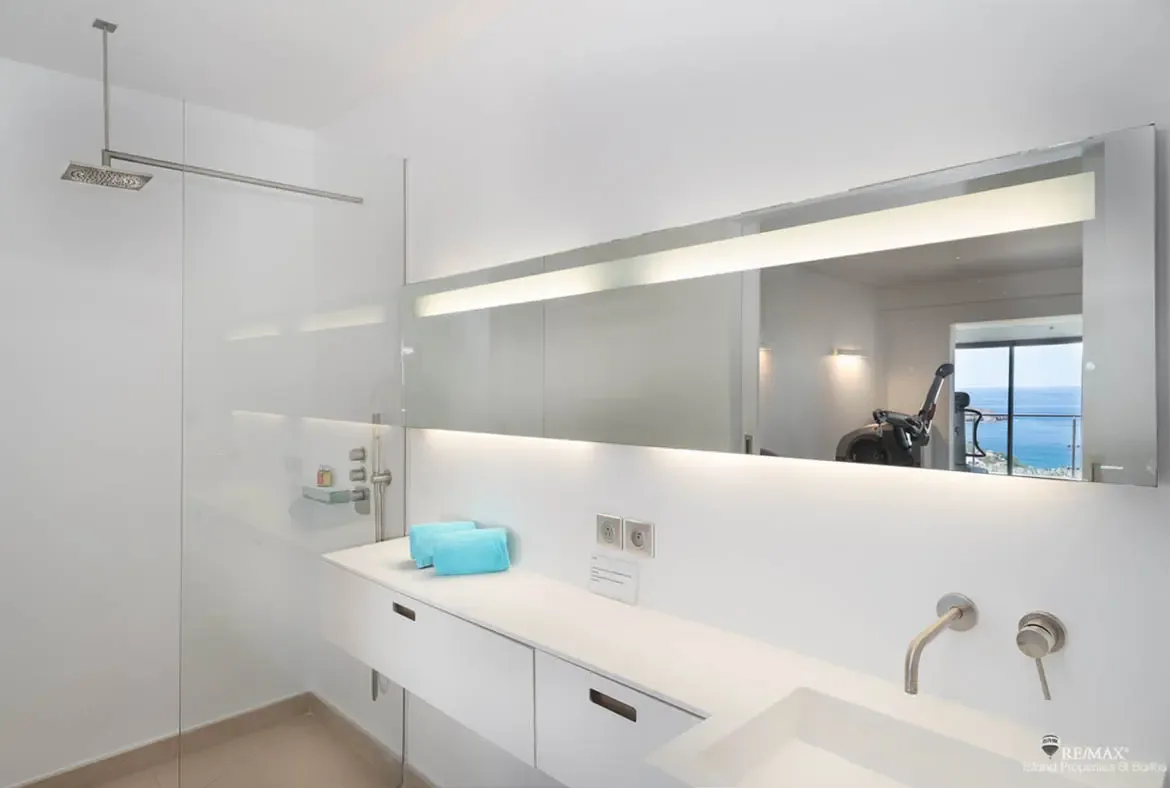 A floating white vanity and sleek glass shower give this bathroom a crisp, modern edge, softened by the glow of the LED mirror and neatly folded blue towels. In the reflection, even the ocean becomes part of the design.