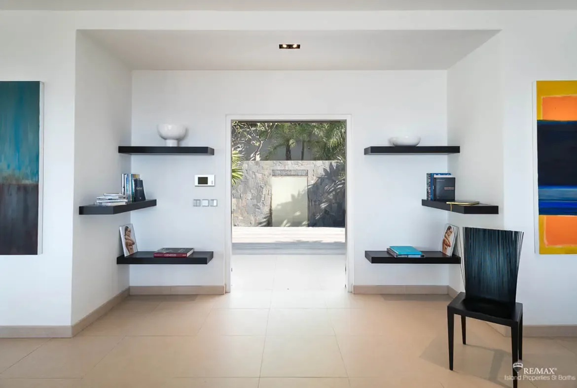 This gallery-like entryway pairs bold contemporary art and floating shelves with a dramatic view straight into a lush tropical courtyard beyond. Clean lines, warm stone floors, and a sculptural black chair make the first impression feel curated and unmistakably modern.