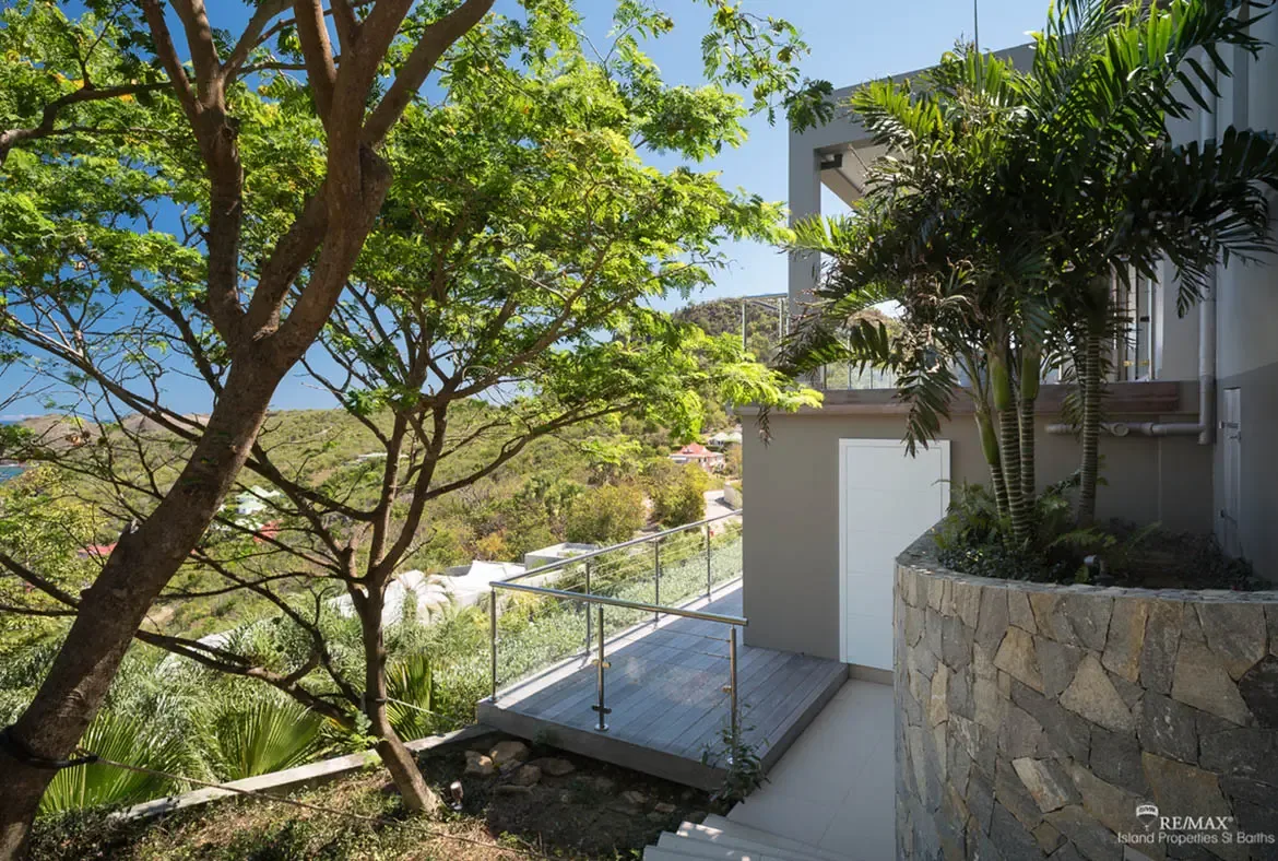 Textured stonework, sunlit terraces, and lush tropical trees give this exterior a sculpted, hillside feel. With glimpses of the sea in the distance and a private deck tucked into the greenery, the setting feels both elevated and secluded.