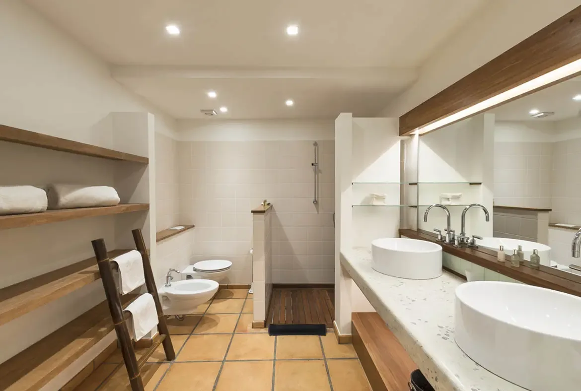 An open walk-in shower with a dark wood slat floor and a double vanity with vessel sinks give this bathroom a clean, spa-like flow, while wooden ladder shelving adds warm texture.