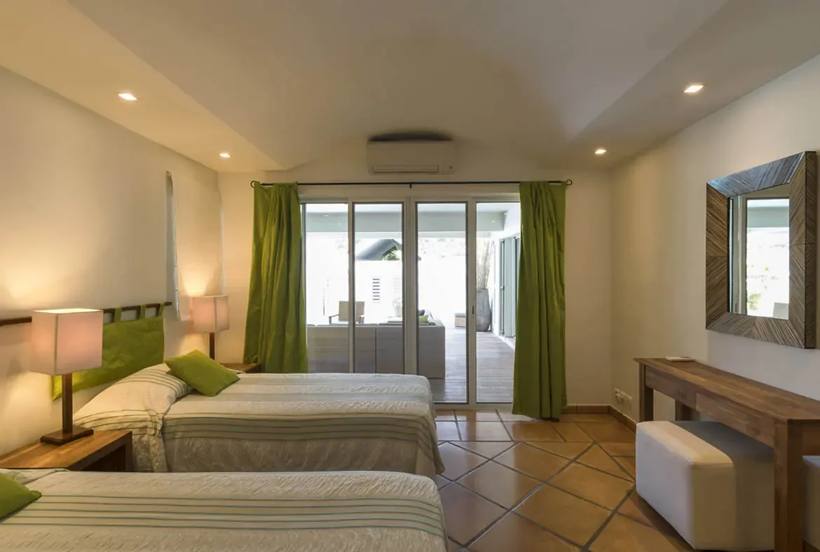 Lime-green headboards and curtains give this twin bedroom a fresh tropical feel, with glass doors opening directly to a sunlit patio surrounded by lush greenery.
