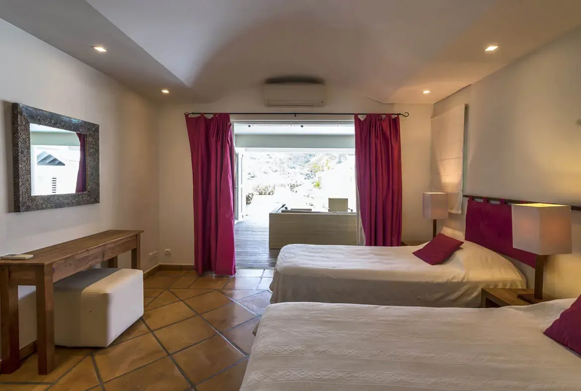 Magenta-padded headboards and matching curtains bring bold color to this twin bedroom with vaulted ceilings, where glass doors open to a sun-drenched wooden deck.