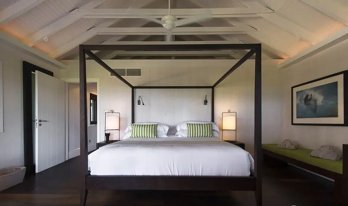 Green-striped pillows and a lime-green bench bring fresh color to this canopy bedroom, where a black-framed ocean wave photograph hangs above and white vaulted rafters add height.