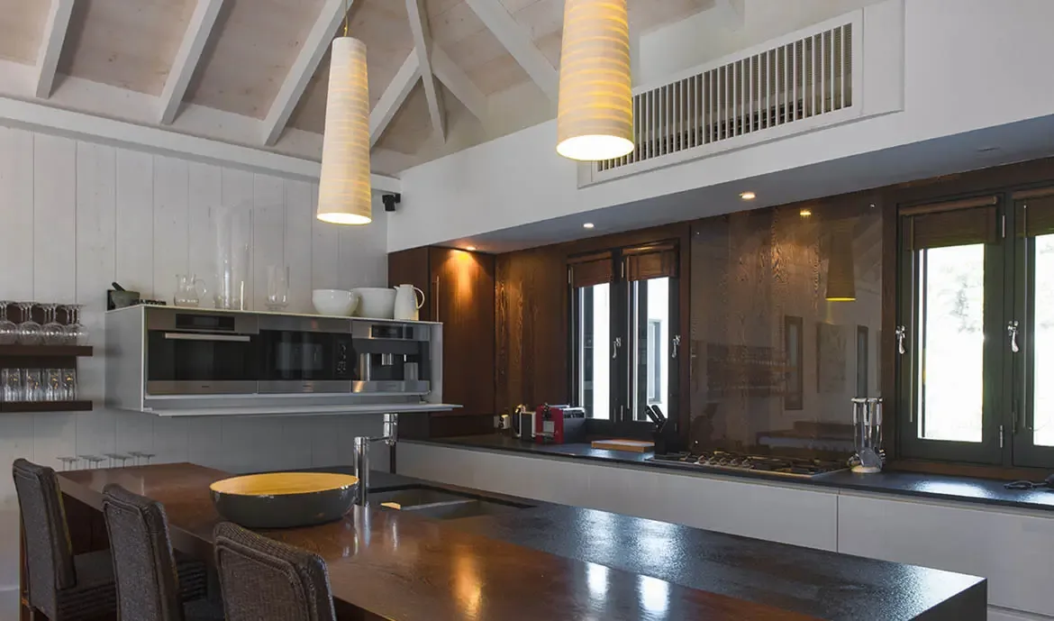 A dark wood island with bar stools anchors this vaulted kitchen, where white paneling, floating shelves, and a red coffee maker add warmth to the contemporary design.