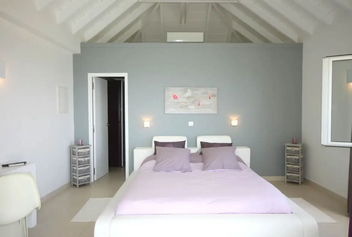 A sanctuary of calm, this modern bedroom features clean lines, soft lilac accents, and soaring vaulted ceilings.