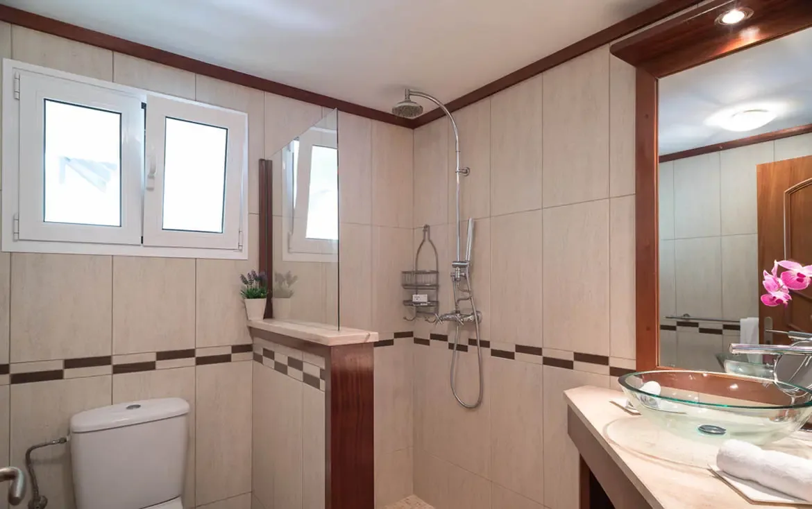 A translucent green glass vessel sink sits on a light vanity with pink orchids, while a walk-in shower with chrome fixtures and a frosted window keeps this bathroom bright and serene.