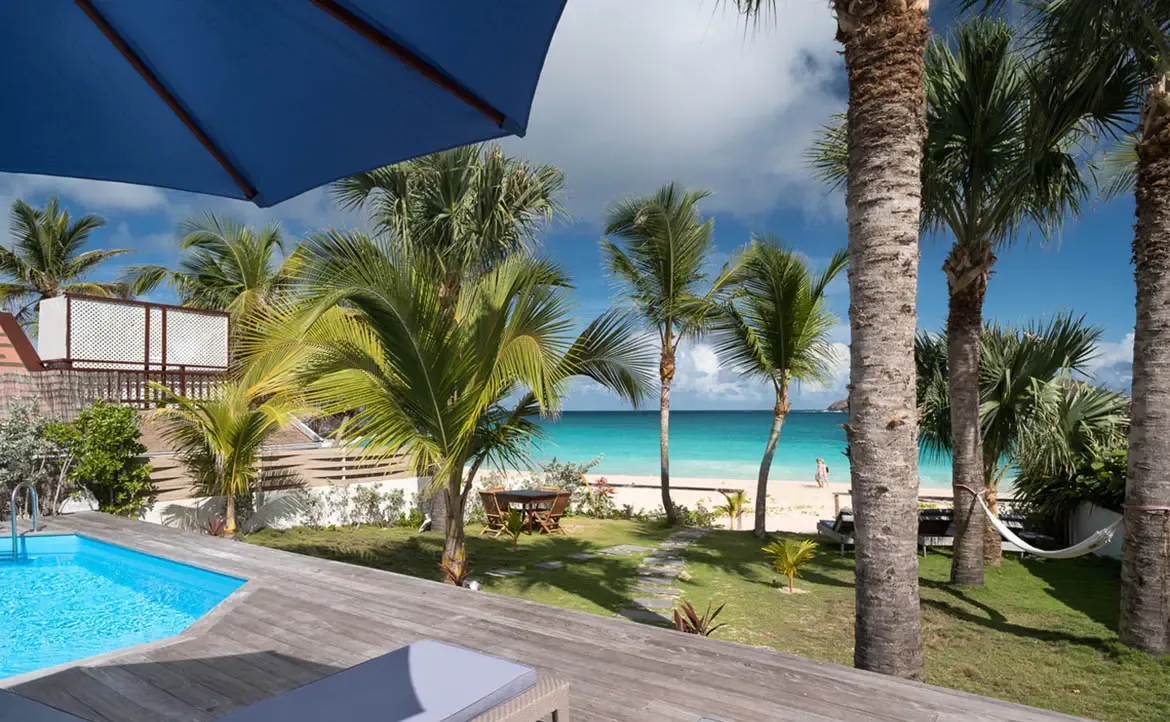 A white hammock between palms and lounge chairs on a green lawn overlook a turquoise pool, where a sandy path leads to a pristine beach and sapphire Caribbean water.