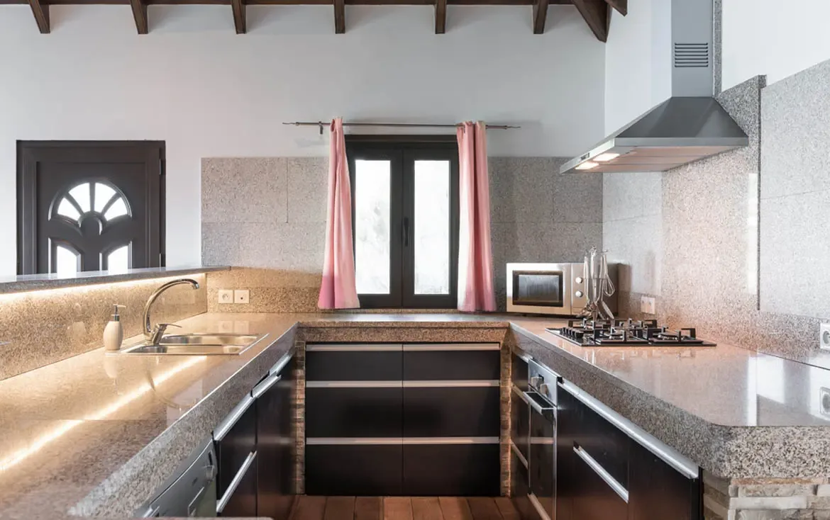 Dark cabinetry and granite countertops wrap around a U-shaped kitchen, where a stainless hood, pink curtains, and dark exposed beams add character to the cook's domain.