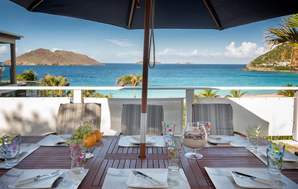 Indulge in an exquisite alfresco dining experience at Villa Gem-Palm Springs, where vibrant table settings meet the serene, turquoise horizon of St. Barths for the ultimate island retreat.