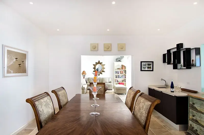 Orange candles in tall glass holders center a dark wood dining table, where a kitchenette with frosted-glass cabinets and a sunburst mirror in the living room beyond.