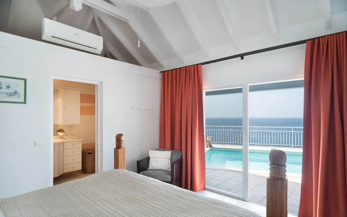 Wake to an uninterrupted ocean view framed by floor-to-ceiling glass. A private turquoise pool awaits just steps from your bed—morning dip before coffee, anyone? Vaulted white ceilings and terracotta curtains complete this seamless indoor-outdoor retreat.