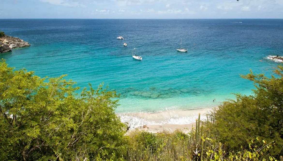 From your hillside perch, the Caribbean unfolds in graduated turquoise to deep indigo. A secluded beach cradles the shore while sailboats anchor in the bay—your private view of paradise, far from the crowds.