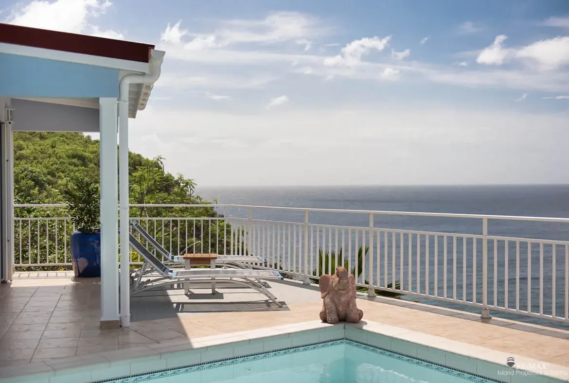 Two modern loungers angle toward the endless ocean horizon, positioned beside a sparkling pool on the sun-drenched terrace. A playful terracotta elephant adds charm while lush hillsides provide seclusion—your private sanctuary above the Caribbean.