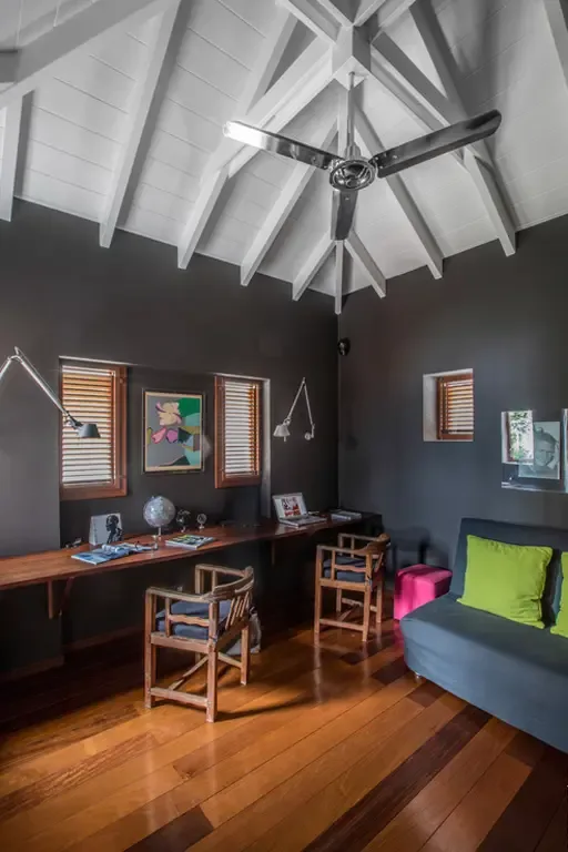 A dedicated study with vaulted white-beamed ceiling and dramatic charcoal walls. Built-in desk, industrial swing-arm lamps, and a gray sofa with lime-green pillows create an inspiring workspace—perfect for a quiet retreat or creative moment.