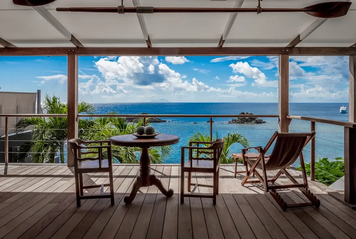 A wooden oar spans the ceiling beams above this intimate terrace, where a pedestal table and lounge chair await. Cable railings vanish before the turquoise-and-sapphire sea—your private nest suspended above the Caribbean, perfect for morning coffee or sunset cocktails.